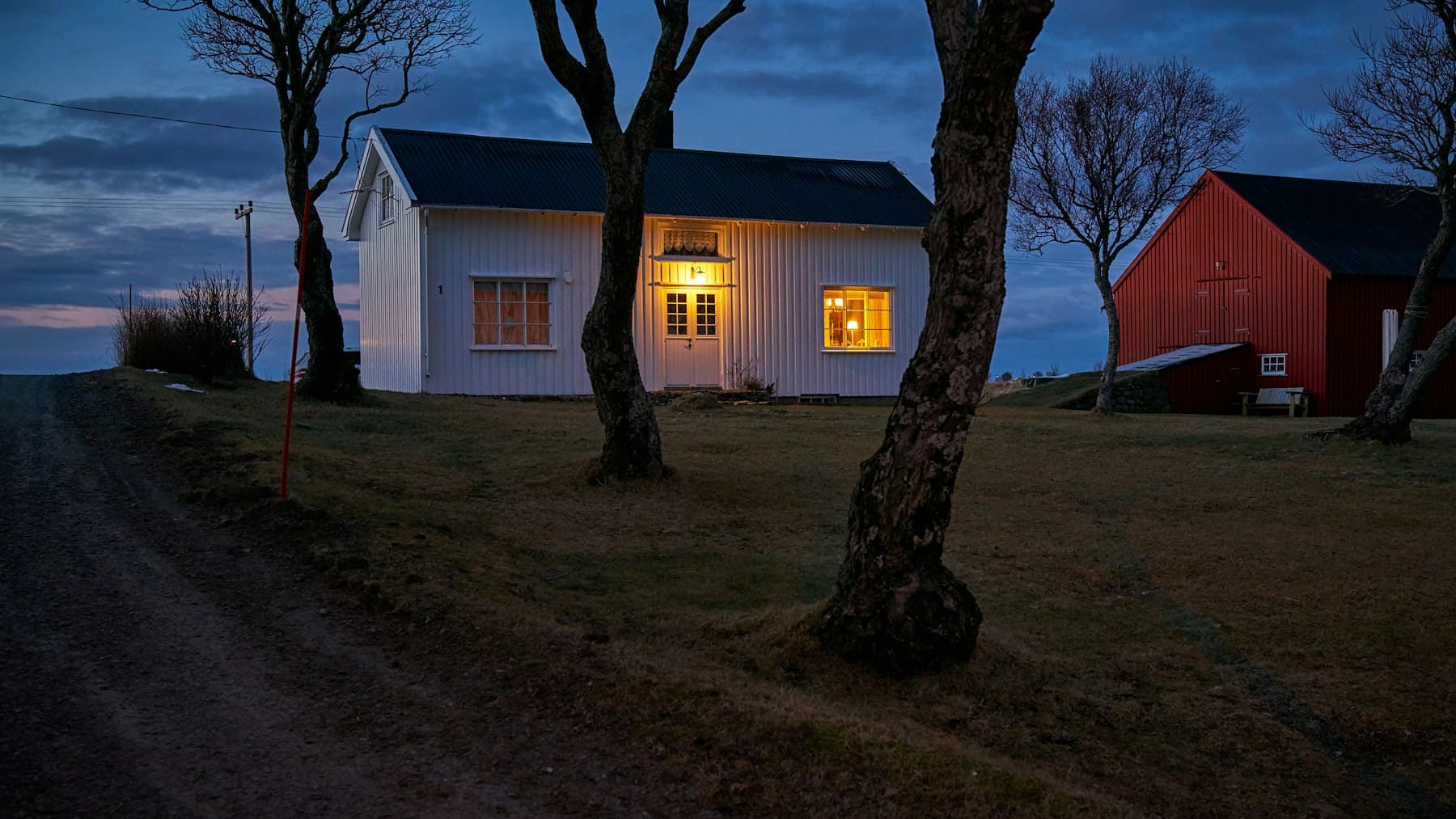 A rural house at dusk with its windows lit from within